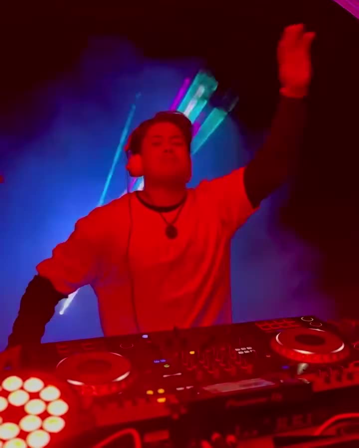 Valdi with one hand up under red and violet lights at a club night