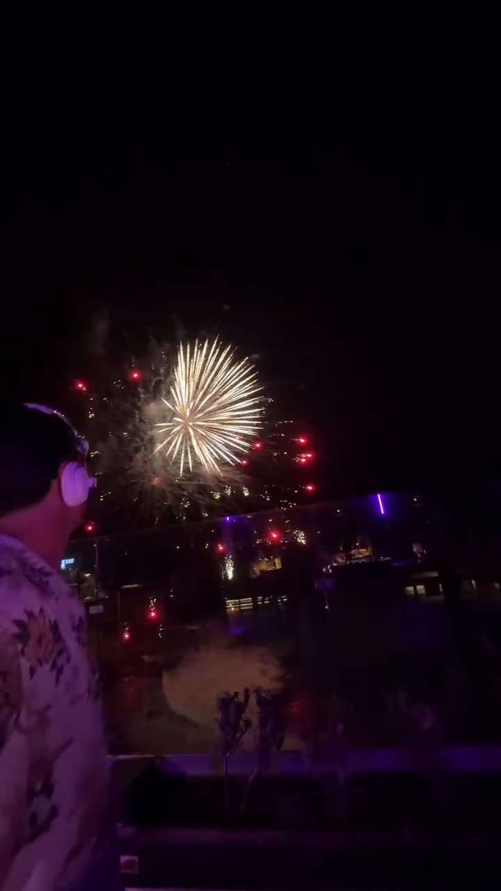 Valdi in headphones at night with fireworks bursting behind him