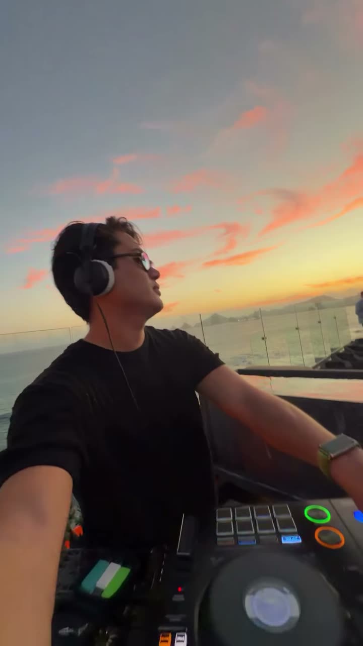 Valdi in headphones at the decks on a terrace at sunset
